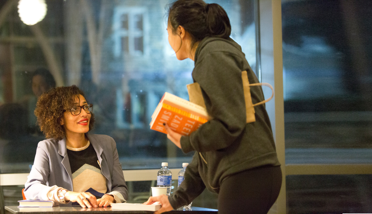 Woman holding books talking to a seated woman.