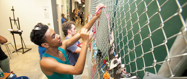 Chain-link canvas: Attendees at the Arts Annex opening reception create a living mural by decorating a fence with materials provided by Durham's Scrap Exchange. Credit: Jared Lazarus