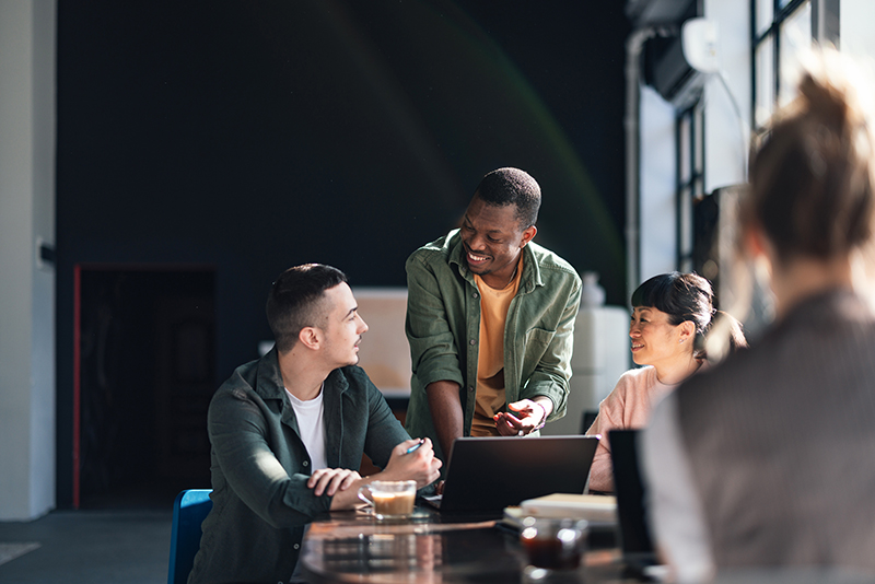 Man standing over two people talking around a laptop.