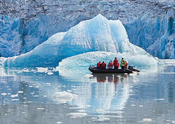 People on inflatable boat in front of glacier ice