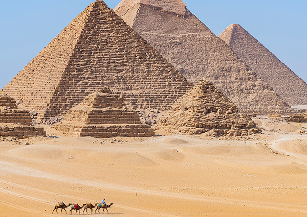 Egyptian pyramids in background with people on camels in foreground