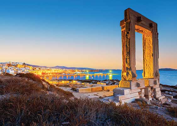 Naxos monument in greece at dusk overlooking city and water in background.