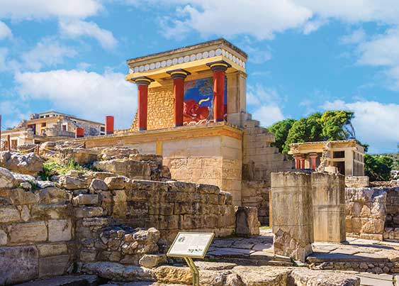 Ancient Palace of Knossos with colorful red pillars and stone rubble.