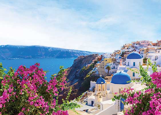 santorini city on the cliffs with body of water in the background and purple flowers in the foreground.